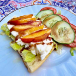 Picture of Burrata - toast with mozzarella on a bed of lettuce with grilled nectarine slices, topped with a drizzle of honey and balsamic vinegar. Also with cucumber and tomato.